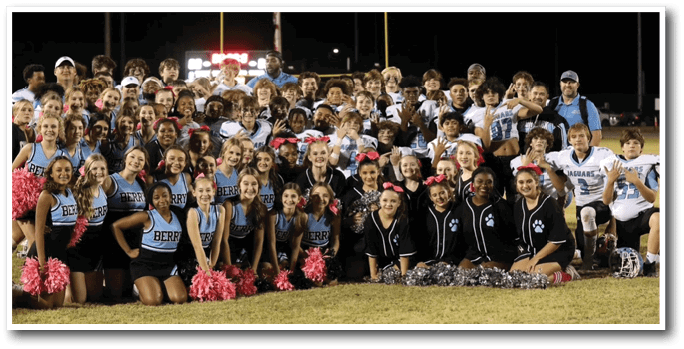 A group of cheerleaders and football players pose for a photo on the field. AI generated content