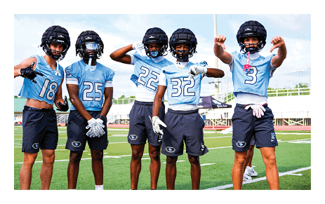 Four football players pose on the field, wearing helmets and jerseys. AI generated content