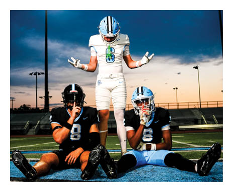 Three football players are sitting on the ground, wearing helmets and uniforms. One player is holding his hands up, while the other two are sitting down. They are all on a field. AI generated content