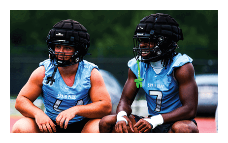 Two men wearing football helmets and uniforms are crouched down on a field. AI generated content