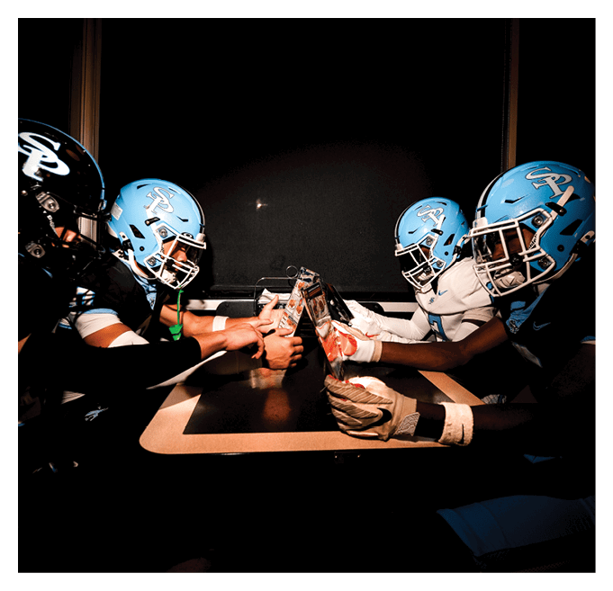 Three football players are sitting around a table, holding their hands together. AI generated content