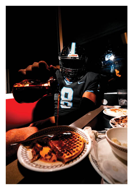 A person wearing a football helmet is sitting at a table with plates of food and a bottle of alcohol. AI generated content
