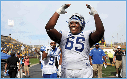 A football player wearing a white jersey with the number 65 on it is celebrating with his teammates. AI generated content