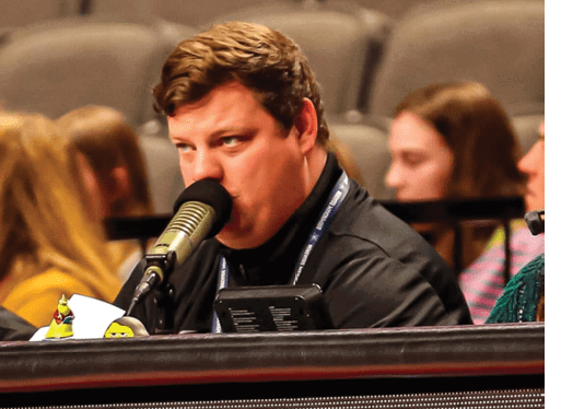 A man wearing a black shirt is sitting at a desk with a microphone in front of him. AI generated content
