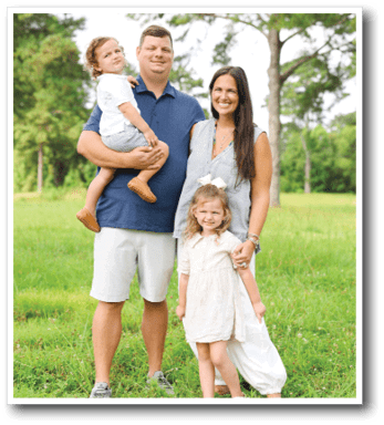 A family of four, including a man, woman, and two children, pose for a photo in a grassy field. AI generated content