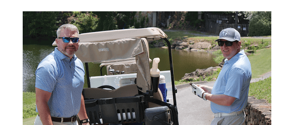 Two men standing next to a golf cart with a cooler and a cup. AI generated content