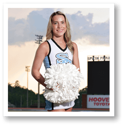 A cheerleader in a blue and white uniform stands on a football field holding a pom pom. AI generated content