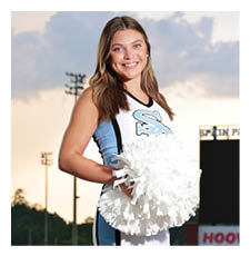 A cheerleader in a blue and white uniform stands on a football field holding a pom pom. AI generated content