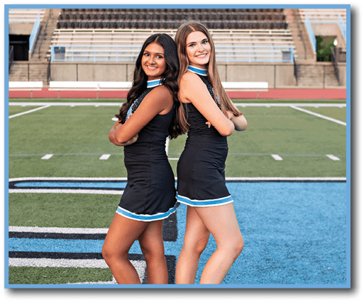 Two cheerleaders pose for a photo on a football field. AI generated content