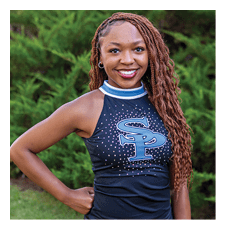 A woman wearing a black and blue cheerleader outfit stands in a grassy field. AI generated content