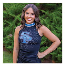 A young woman wearing a black and blue cheerleading outfit stands in front of a bush. AI generated content