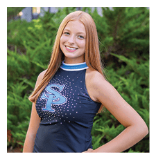 A young woman wearing a black and blue cheerleader outfit stands in front of a bush. AI generated content