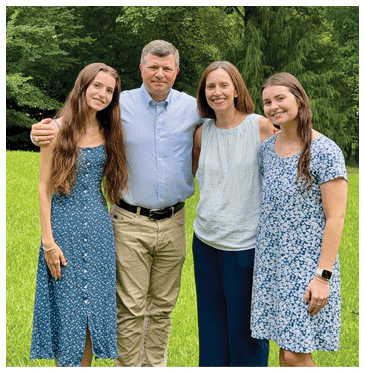 A man and three women pose for a picture in a grassy field. AI generated content