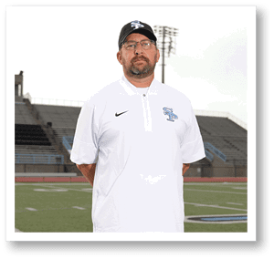 A man wearing a white shirt and a cap stands on a football field. AI generated content