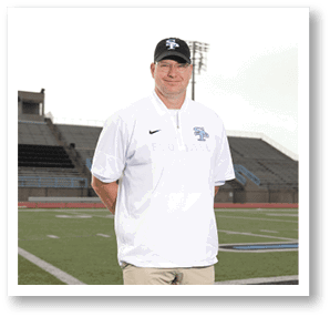 A man wearing a white shirt and a black hat stands on a football field. AI generated content