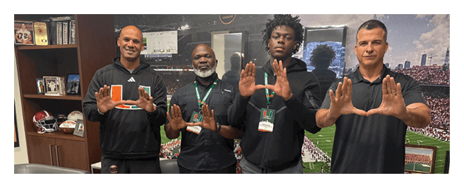 Four men pose in front of a table with footballs and a statue. AI generated content