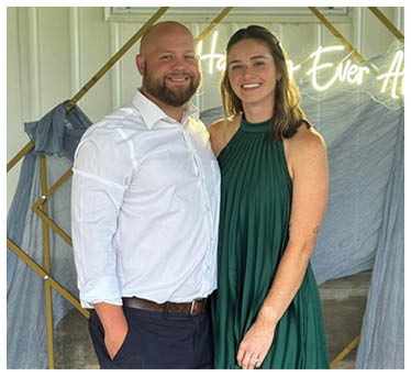 A man and woman pose for a picture in front of a sign that says “Happy Ever After." AI generated content