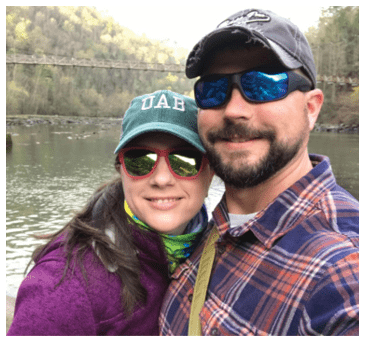 A man and woman are standing together on a bridge, posing for a picture. The woman is wearing a green hat and sunglasses, and the man is wearing a plaid shirt. AI generated content