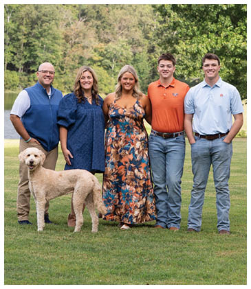 A group of five people and a dog pose for a picture in a grassy field. AI generated content