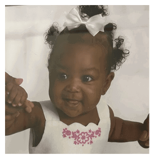 A baby girl wearing a white dress with pink flowers is being held by a woman. AI generated content