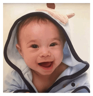 A baby wearing a blue and white hoodie is smiling and sitting on a bed. AI generated content