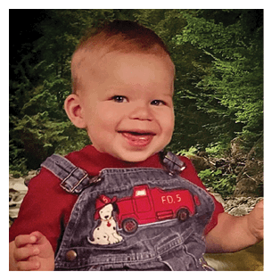 A young child wearing a red shirt and blue overalls is smiling and sitting in front of a green background. AI generated content