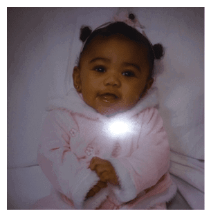 A baby wearing a pink snowsuit and a white hat is sitting on a bed. AI generated content