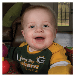 A baby wearing a Green Bay Packers jersey is sitting on a couch. AI generated content