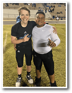 Two young men are standing on a field, posing for a picture. One of them is wearing a black shirt and the other is wearing a white shirt. They are both holding their hands on their shoulders. AI generated content