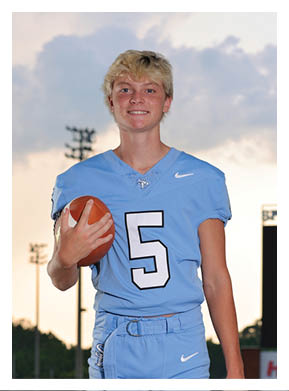 A young man wearing a blue football uniform stands on a field holding a football. AI generated content