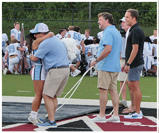 A group of people are standing on a field, some of them are wearing blue shirts. A woman is hugging a man in a blue shirt. AI generated content