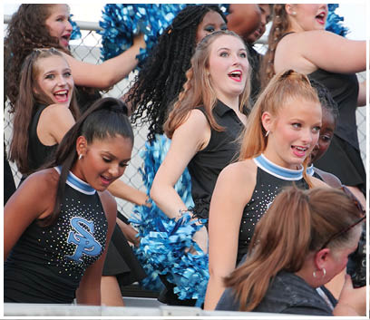 A group of cheerleaders in uniforms are standing on a field, smiling and posing for a picture. AI generated content