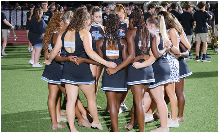 A group of cheerleaders huddle together on a field. AI generated content