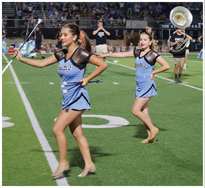 Three female cheerleaders in blue uniforms are standing on a football field. AI generated content