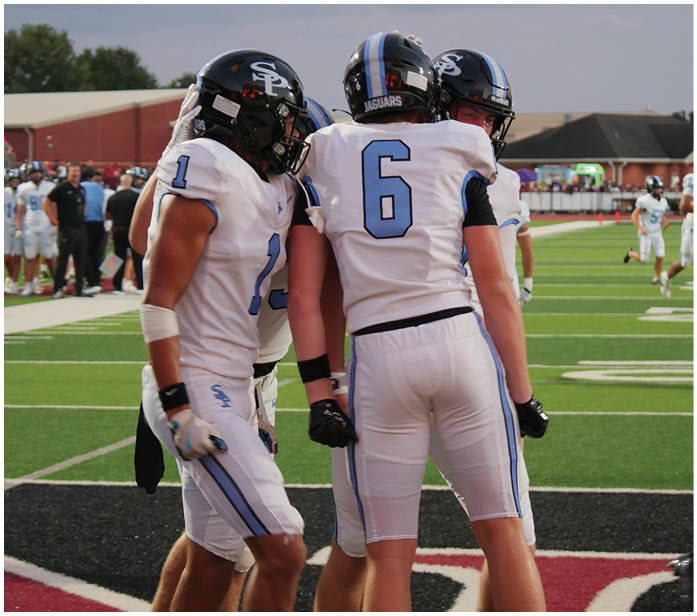 Three football players wearing white uniforms and blue numbers on their backs stand on a field. AI generated content
