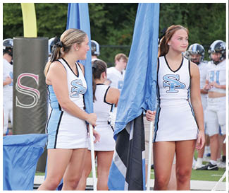 Two cheerleaders holding flags on a field. AI generated content
