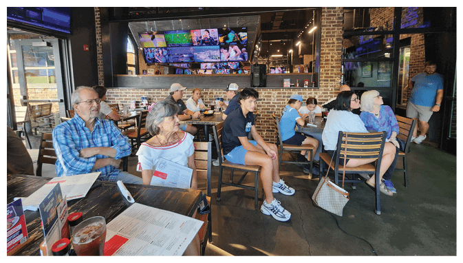 A group of people are sitting in a restaurant, watching TVs on the wall. AI generated content