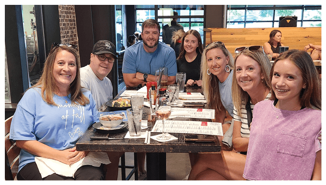 A group of people are sitting around a table in a restaurant, enjoying a meal together. AI generated content