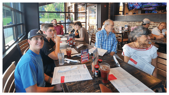 A group of people are sitting at a restaurant table, enjoying their meal. AI generated content
