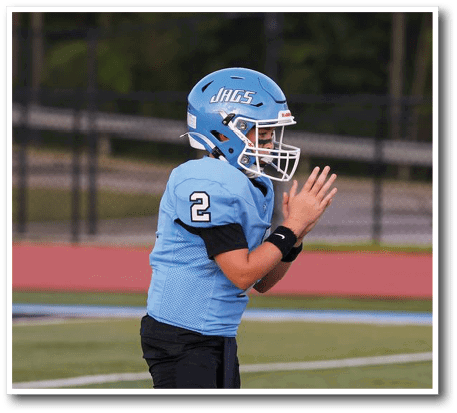A young boy wearing a blue football jersey stands on a field, holding his hands together in prayer. AI generated content