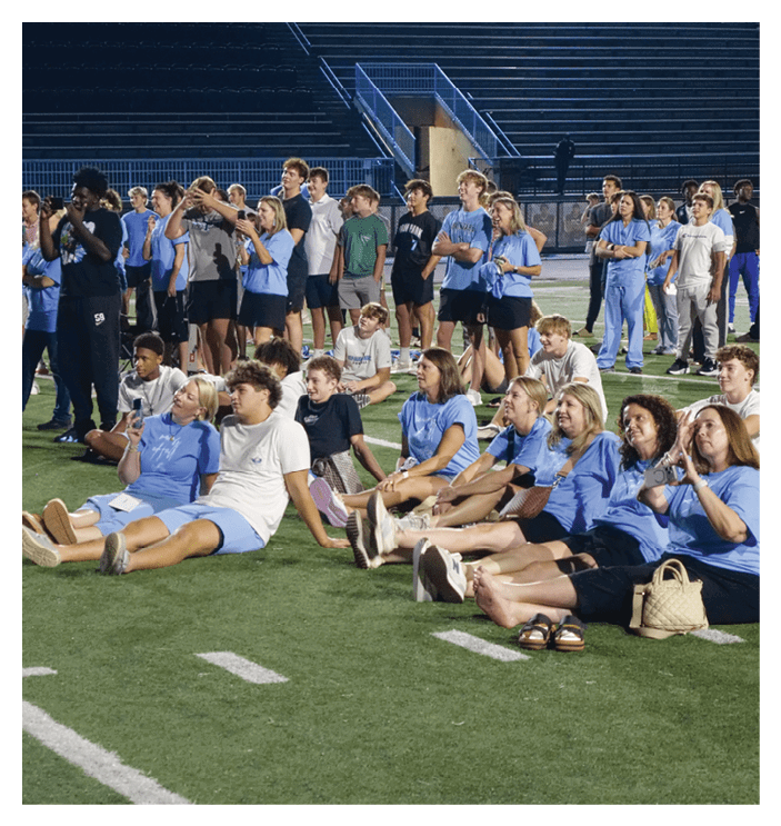 A group of people are sitting on a field, some of them holding drinks. AI generated content