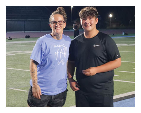 A man and woman are standing on a field, both wearing black shorts. The woman is wearing a blue shirt and has a tattoo on her arm. AI generated content