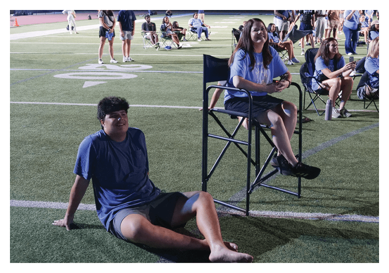 Two people are sitting on chairs on a field. One person is sitting on a stool, while the other is sitting on a chair. They are both smiling and appear to be enjoying their time together. AI generated content