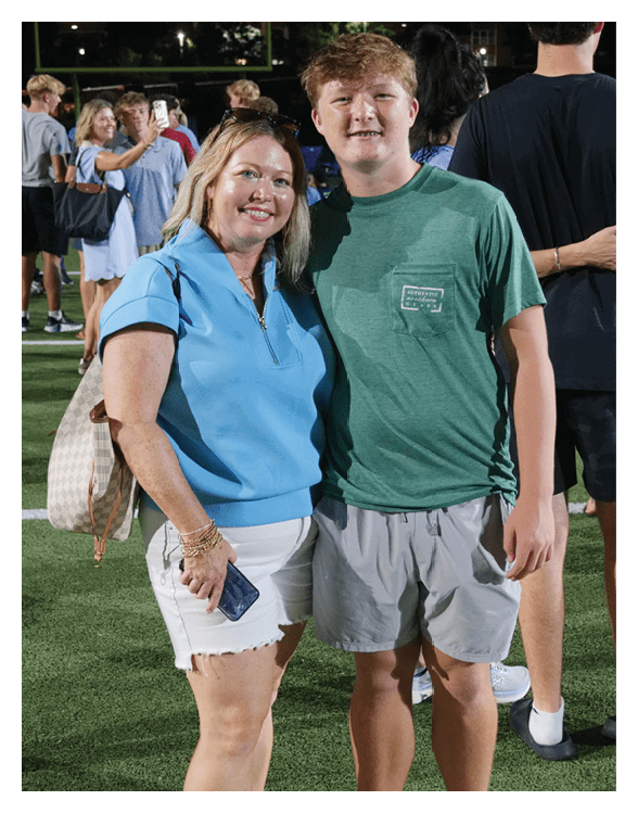 A woman and a boy are standing on a field, posing for a picture. The woman is wearing a blue shirt and holding a purse. The boy is wearing a green shirt. AI generated content