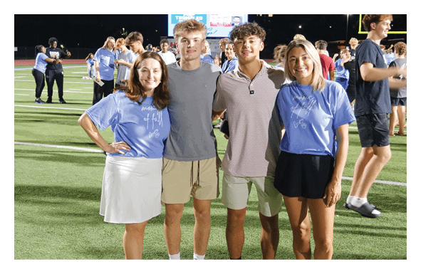 Four people are standing on a field, posing for a picture. They are all wearing blue shirts. AI generated content