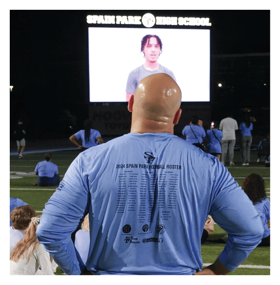 A man wearing a blue shirt and black shorts stands on a field with his hands on his hips. AI generated content