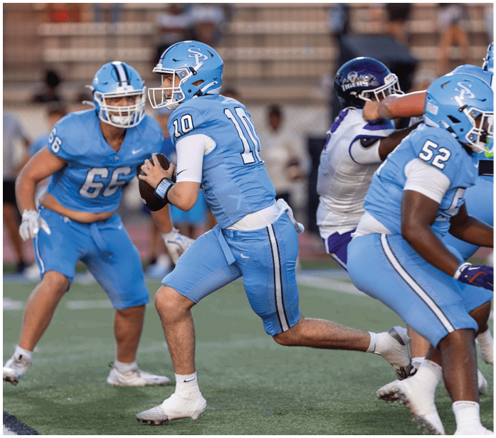 Three football players in blue uniforms are running on a field. One player is holding a football. AI generated content