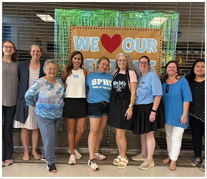 A group of women pose for a picture in front of a sign that says “We love our teachers". AI generated content
