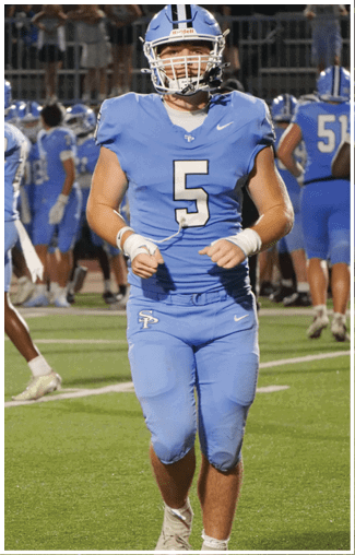 A football player wearing a blue jersey with the number 5 on it walks across the field. AI generated content