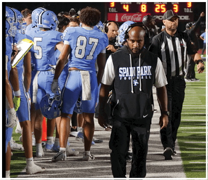 A football team is on the field, with a man in a black shirt and white hat standing in front of them. The man appears to be a referee, and the team members are wearing blue uniforms. The referee is holding a whistle, ready to make a call. AI generated content